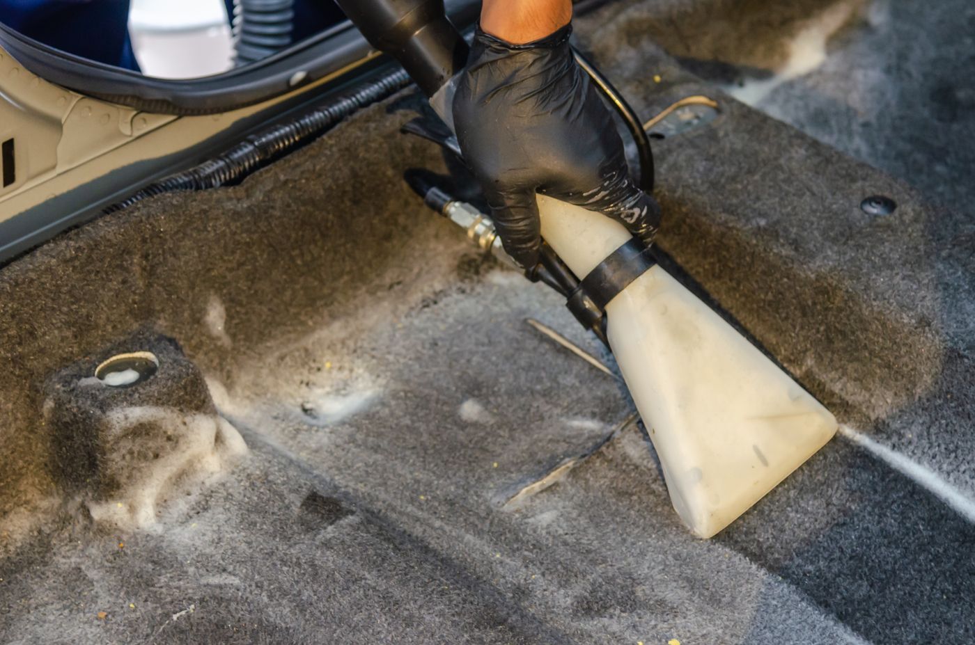 A technician deep cleaning a car footwell carpet with a professional steam extraction tool
