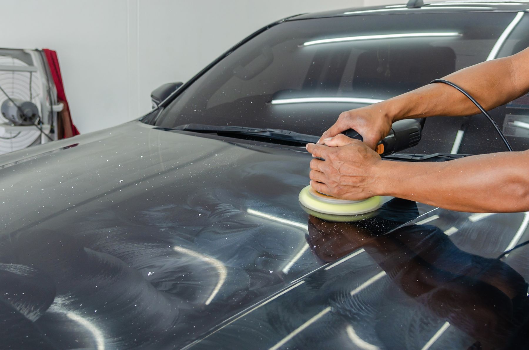 A technician machine-polishing the bonnet of a dark car to a mirror finish